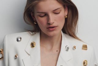 Woman wears white suit pinned with several Heaven Mayhem gold and silver earrings.