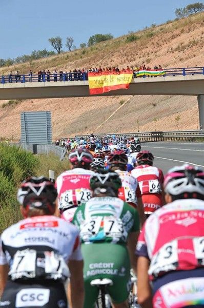 Fans watch the race approaching from a highway overpass.