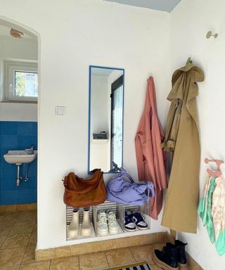 A small entryway with two long coats, a striped shoe rack, and a blue framed mirror