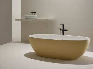 A beige bathroom with a Victoria + Albert bath in Dune Retreat yellow and a white sink.