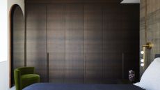 A bedroom with dark wood cupboards, bedside gold sconces and a green sofa chair