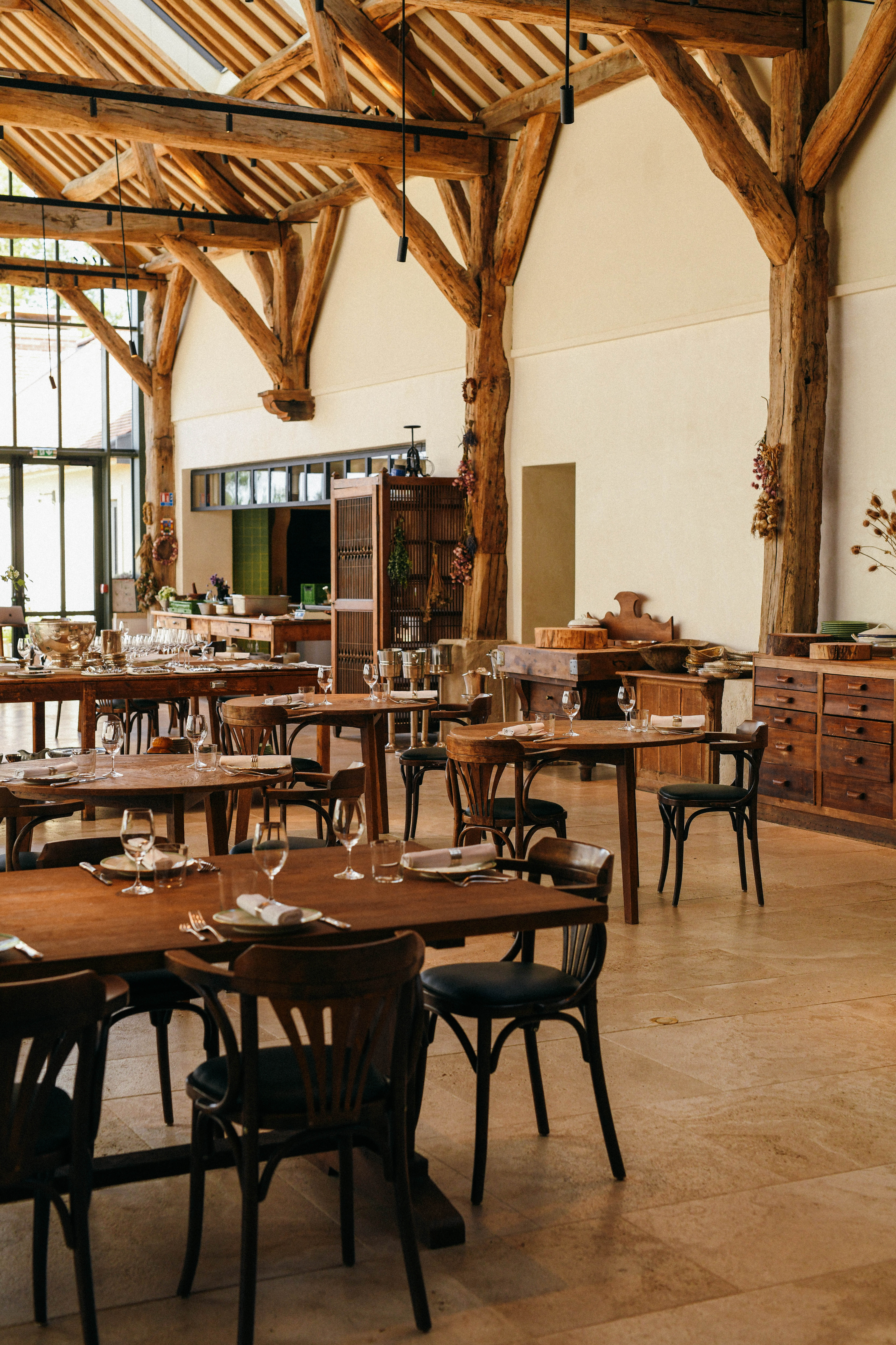 A modern rustic restaurant sited inside an old barn features bistro-style furniture in wood and exposed beams.