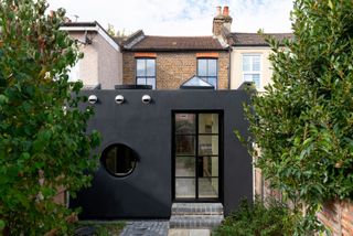 unique terraced house extension with an all-black exterior, black crittall doors, and a small porthole window