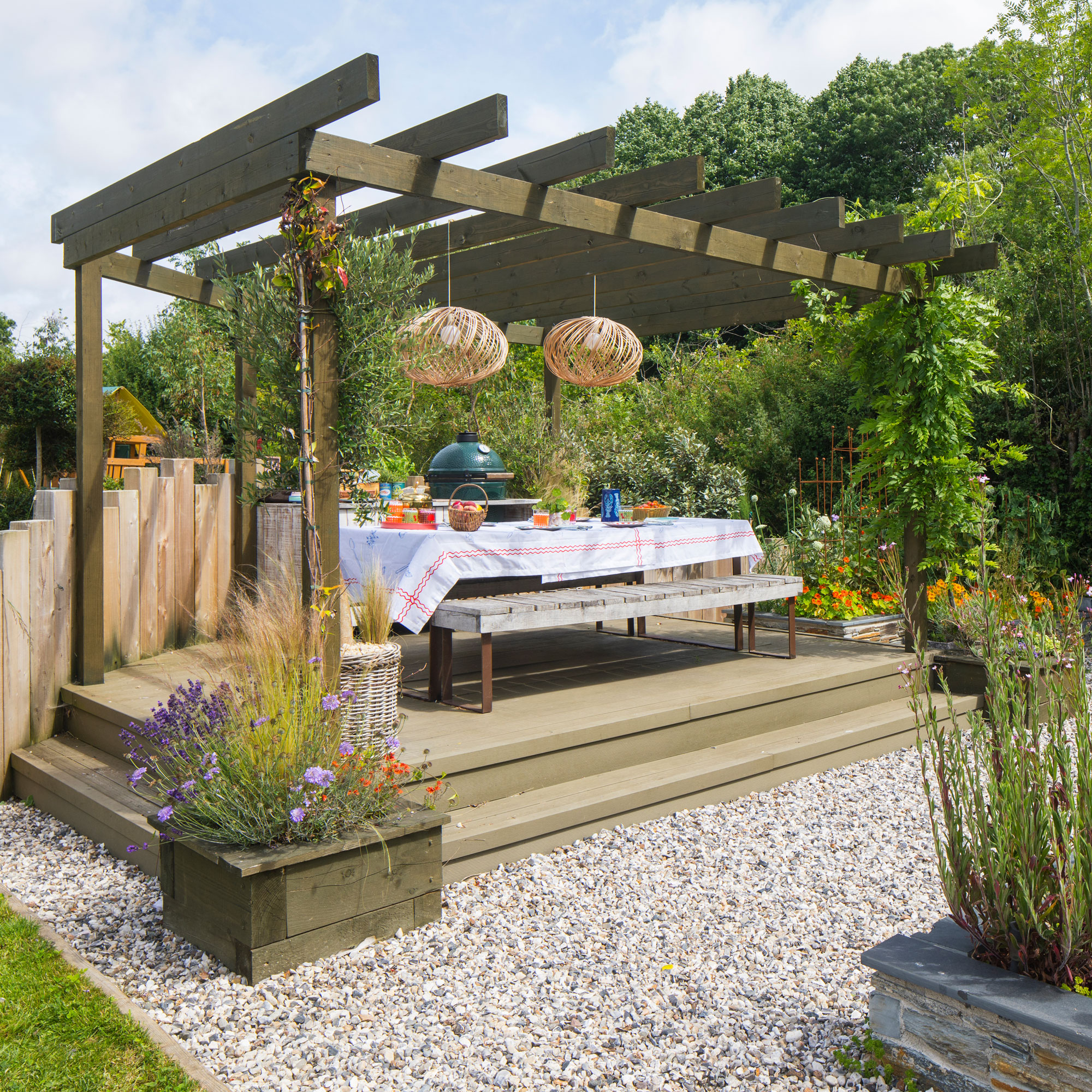 Garden with wooden pergola over wooden deck and lights having over the dining table.