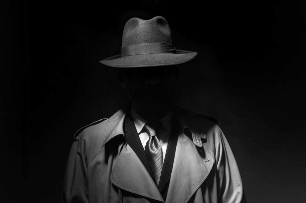 Man in fedora and trenchcoat with shadowed face