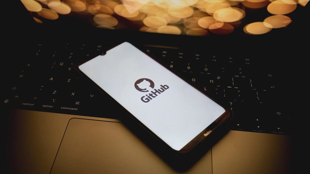 GitHub logo on a mobile phone scren sitting on a macbook keyboard with orange lit screen