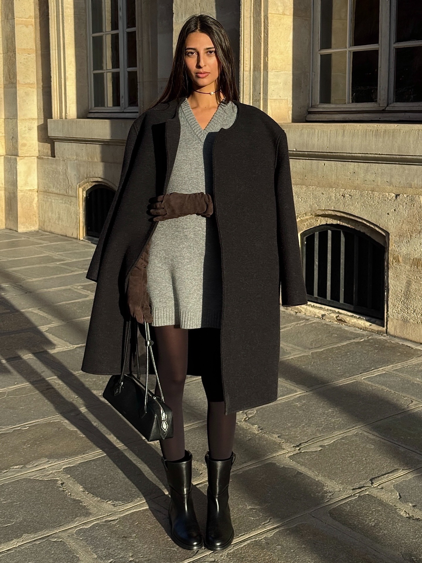 Woman in a black coat, gray knit dress, wearing a black elegant bag