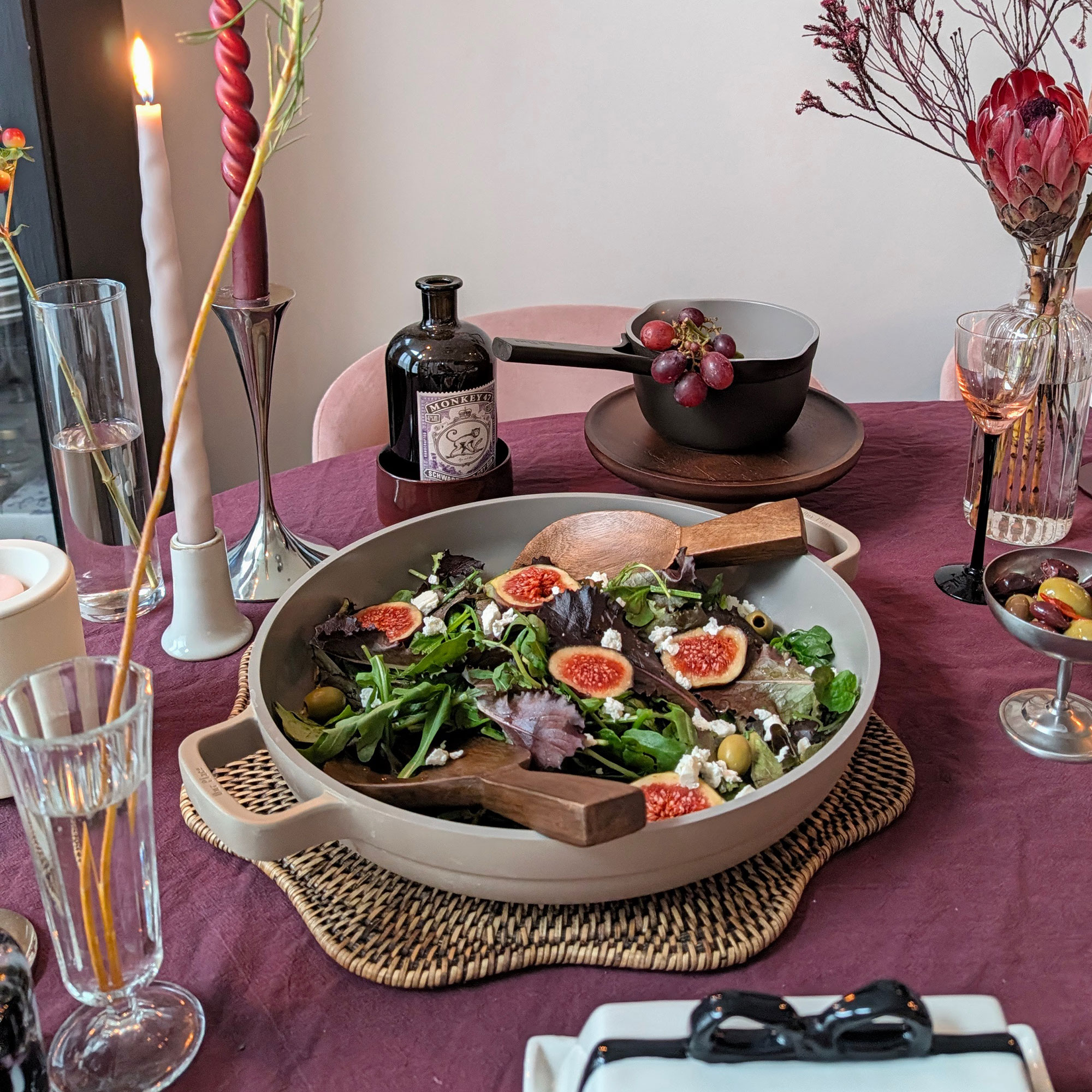 Saute pan filled with salad on woven placemat n top of burgundy table cloth