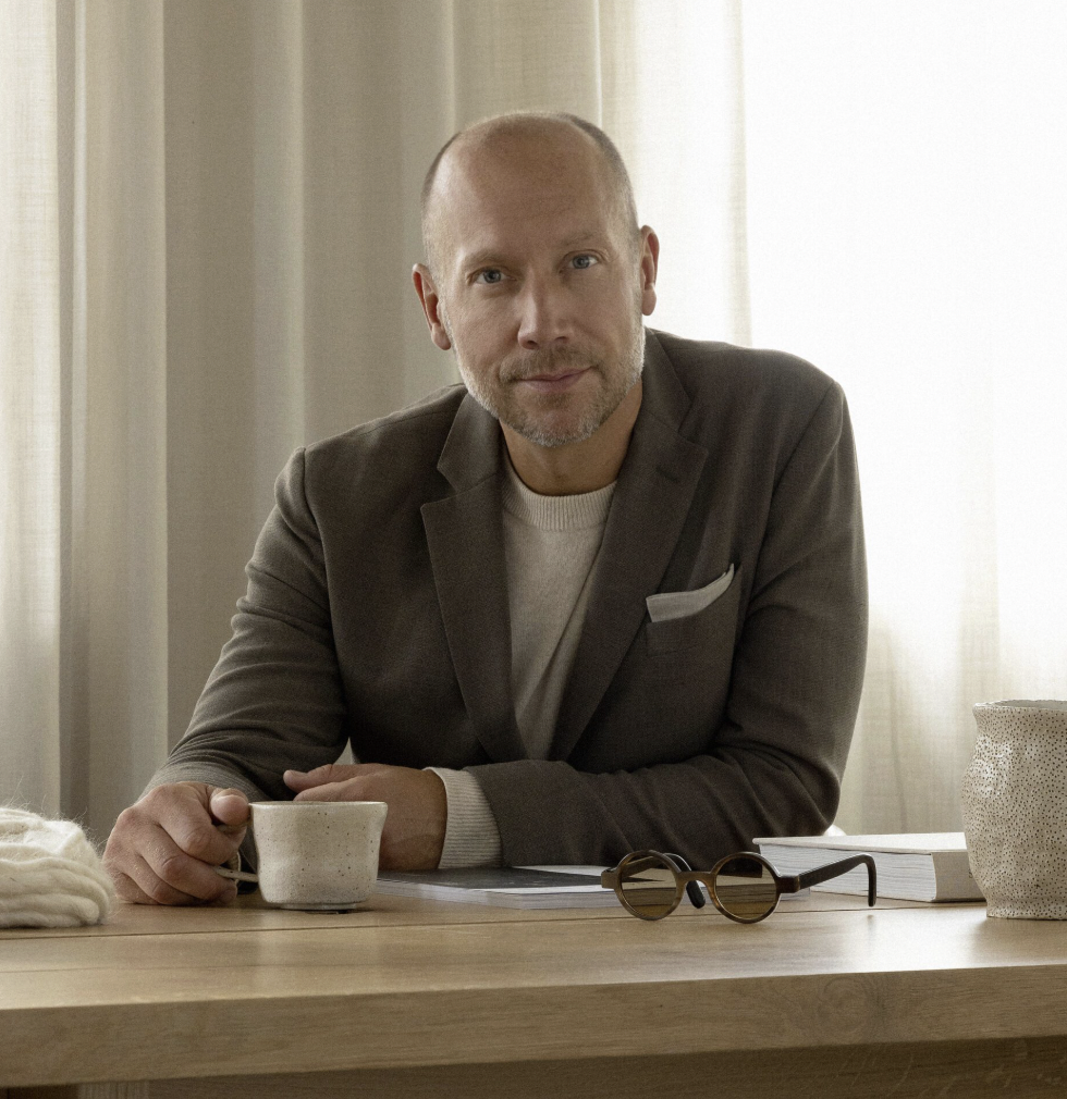 A white man in a smart tailored suit sat at a desk