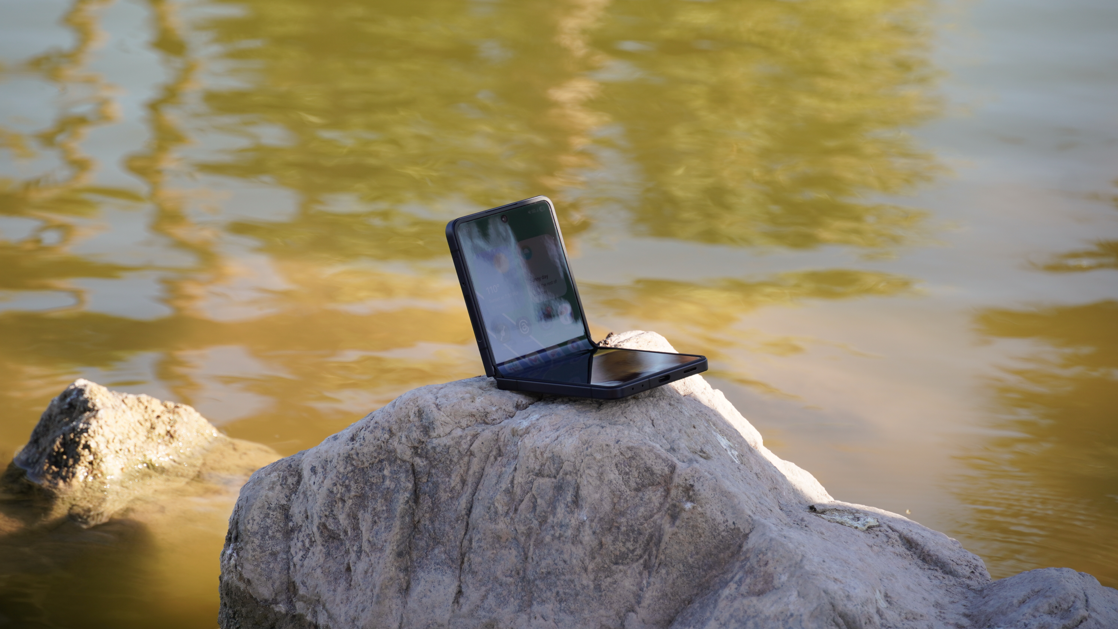 The Samsung Galaxy Z Flip 7 half-opened on a rock in a lake.