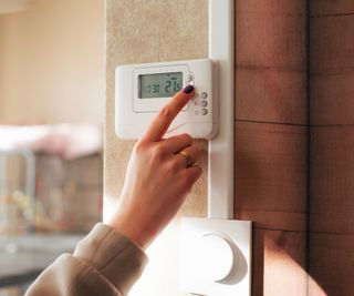 female hand adjusting white wall mounted central heating thermostat