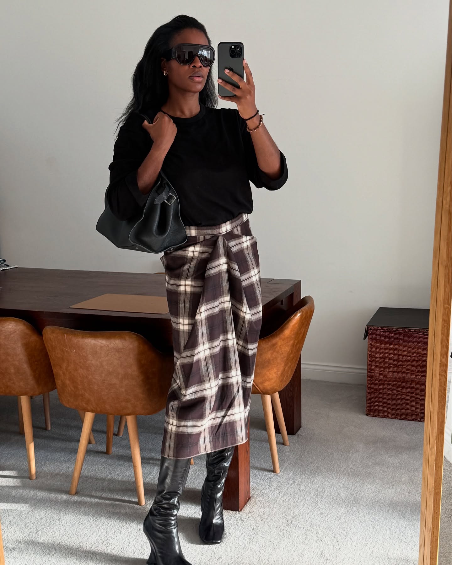 An image of @nlmarilyn wearing a tartan skirt, one of the biggest autumn 2025 skirt trends, with black boots and a black long-sleeve shirt.