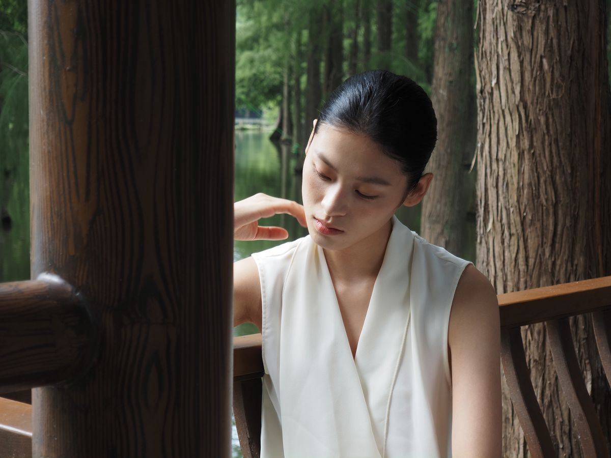OM System PEN sample gallery: Female model in white dress leaning against a wooden barrier in a nature reserve in China