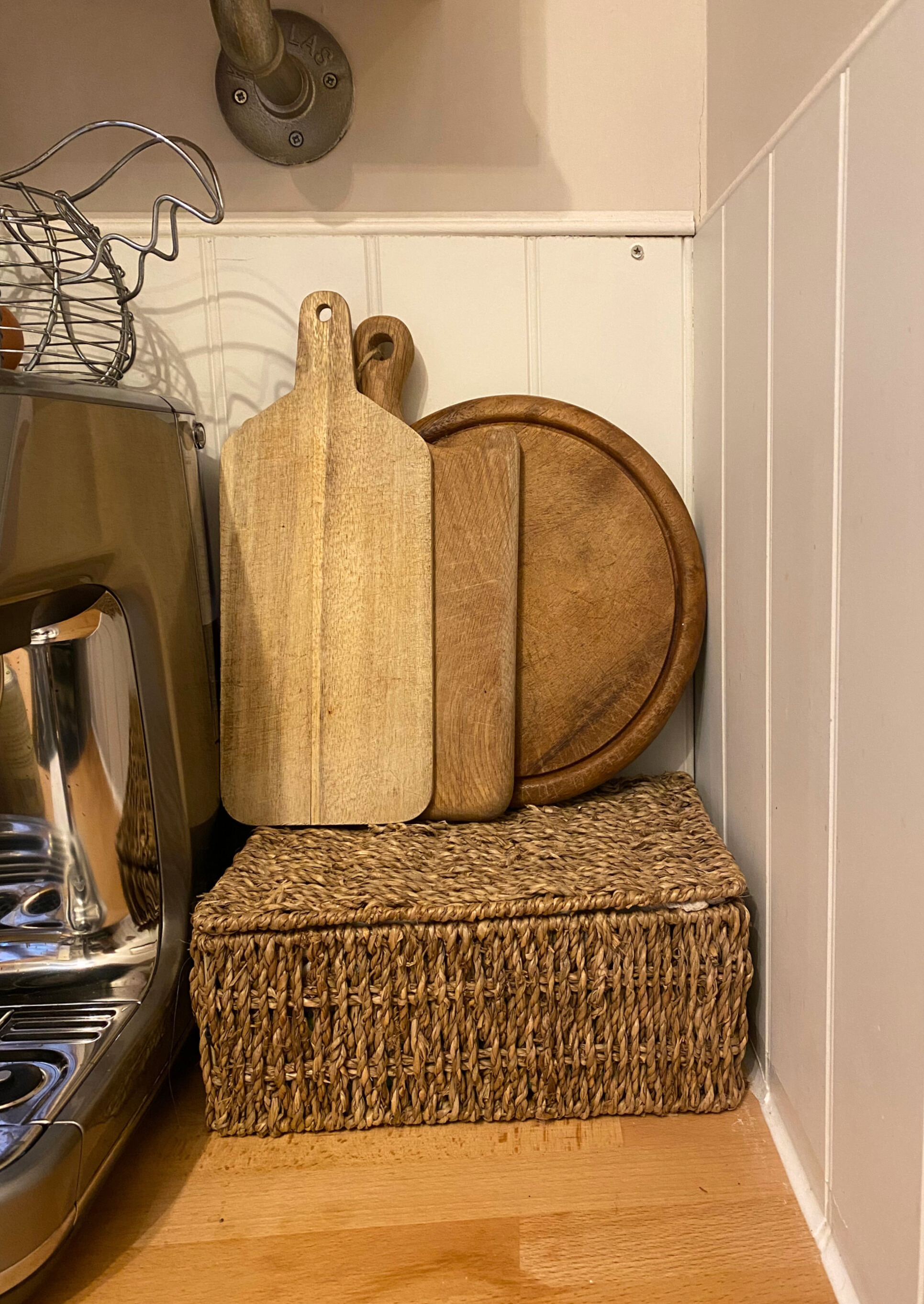 Close up of a kitchen storage basket and chopping boards against a tongue and groove wood panelled backsplash