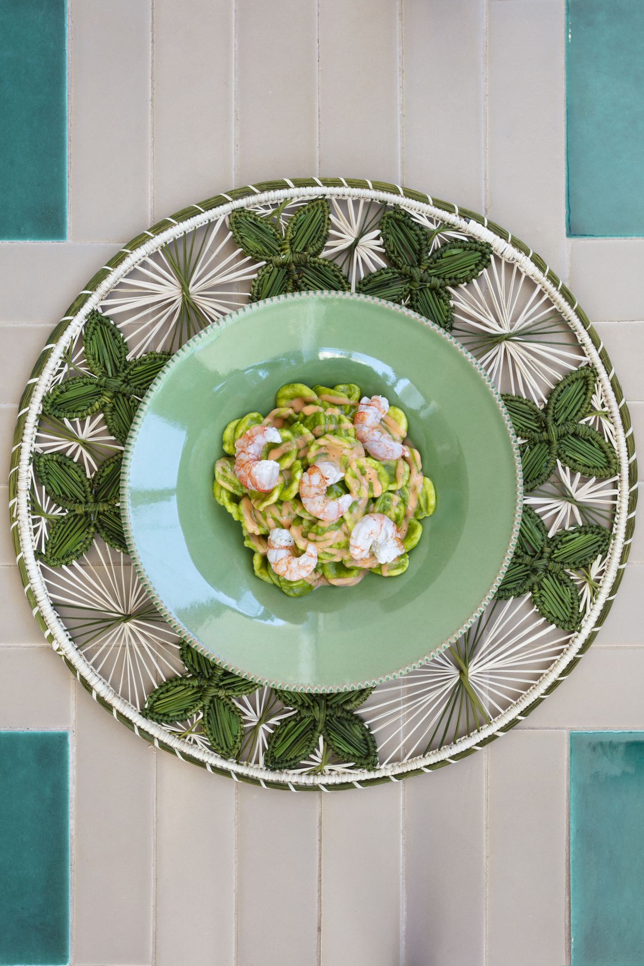 An above look at a pasta dish served in a seagreen plate and filled with shrimps and green cream.