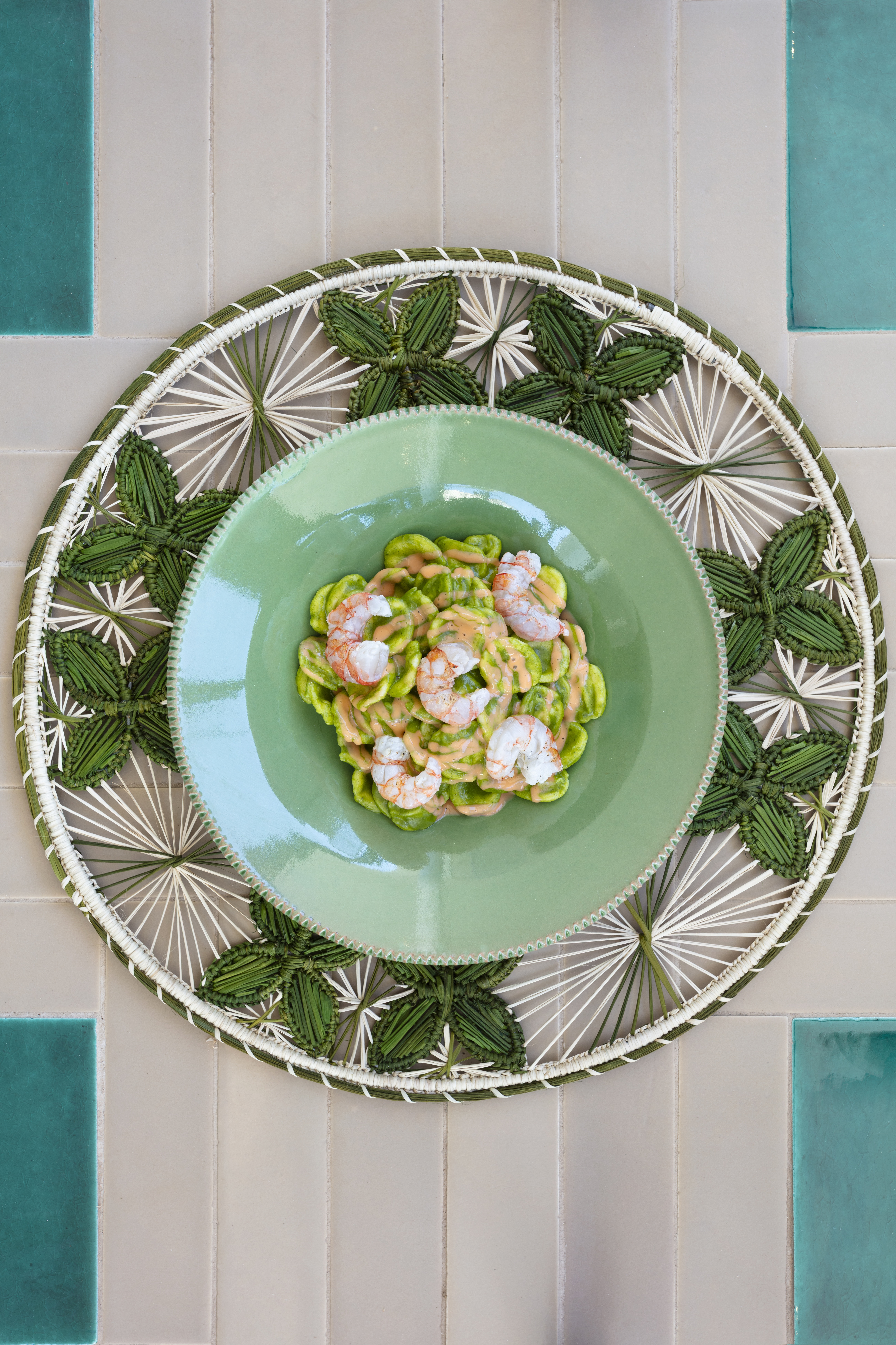 An above look at a pasta dish served in a seagreen plate and filled with shrimps and green cream.