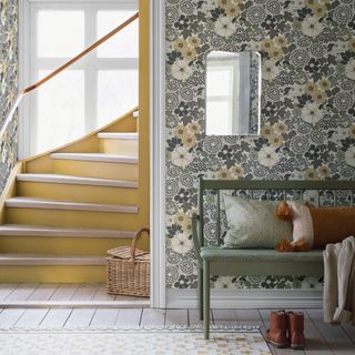 a wallpapered hallway with a stairwell to one side and a bench with cushions