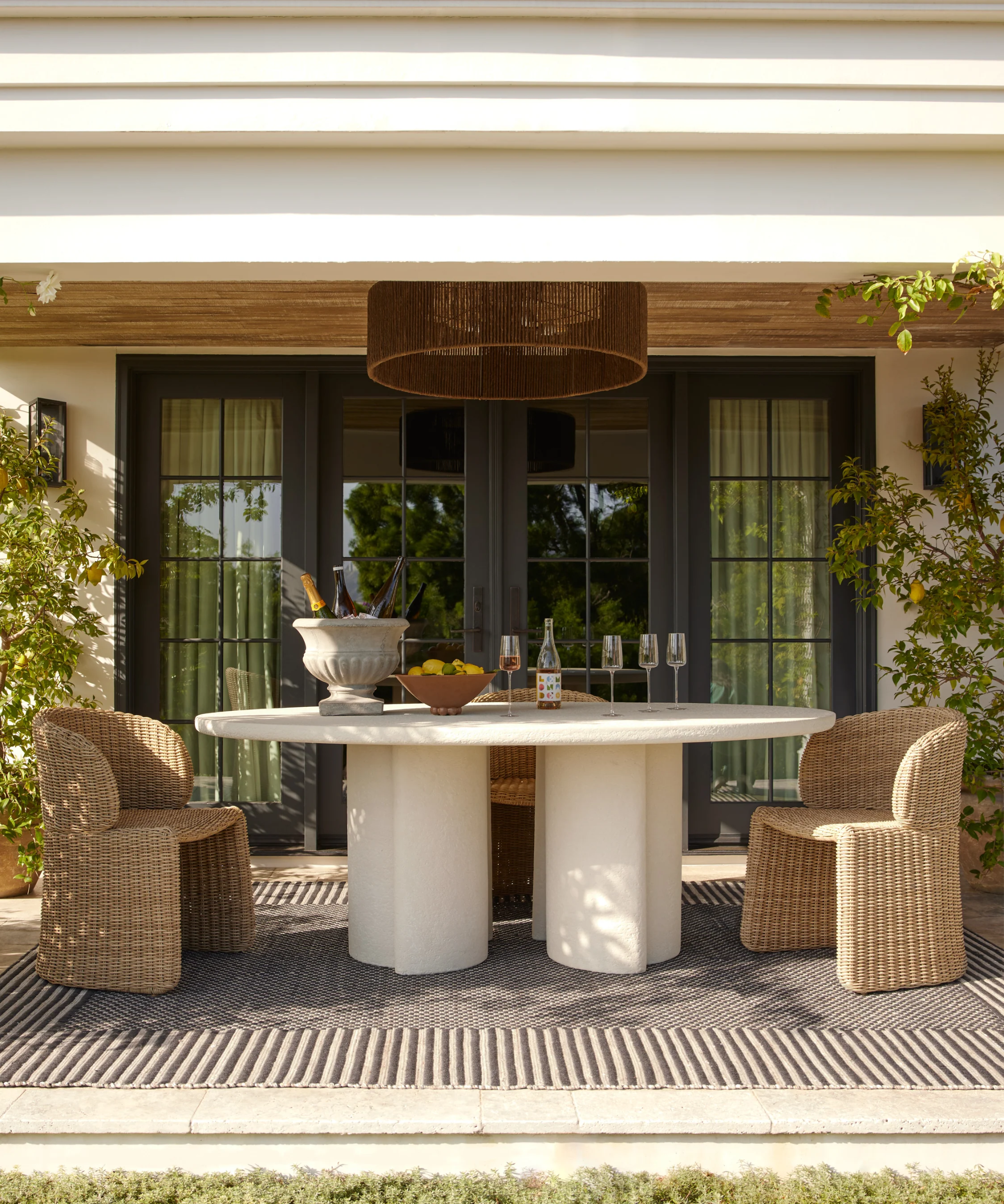 an outdoor dining scene with a large table and two woven chairs underneath a covered porch