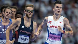 Josh Kerr (L) of Team Great Britain, in a navy blue vest and sunglasses, races Jakob Ingebrigtsen of Norway, in a white vest and blue shorts, in the 1500m at the 2024 Paris Olympic Games.