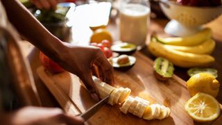 Woman chopping up banana on wooden chopping board to prepare healthy smoothie