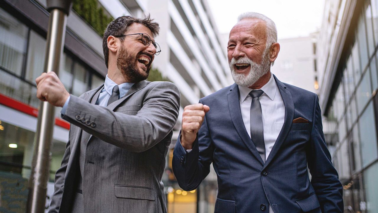 Two businessmen, one young man and the other an older man, joke together.