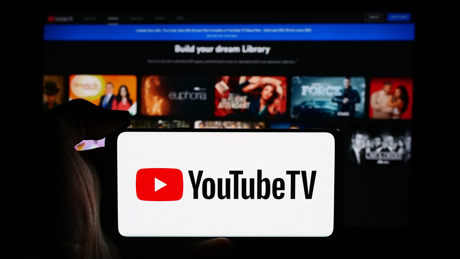 A person is holding a cellphone with the logo of YouTube TV in front of the business webpage