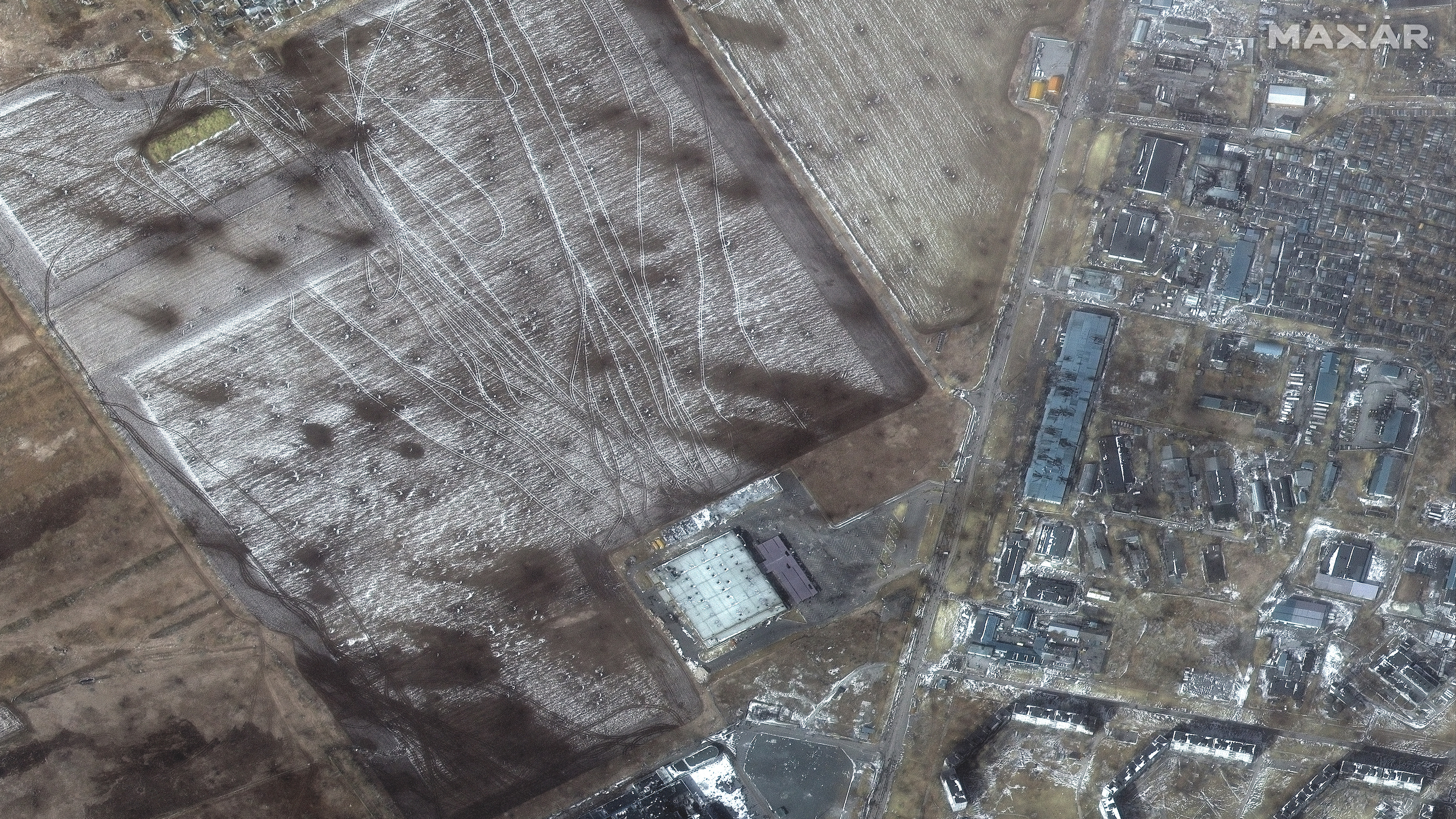 A cratered field, traced with trackmarks, is pictured next to destroyed buildings.