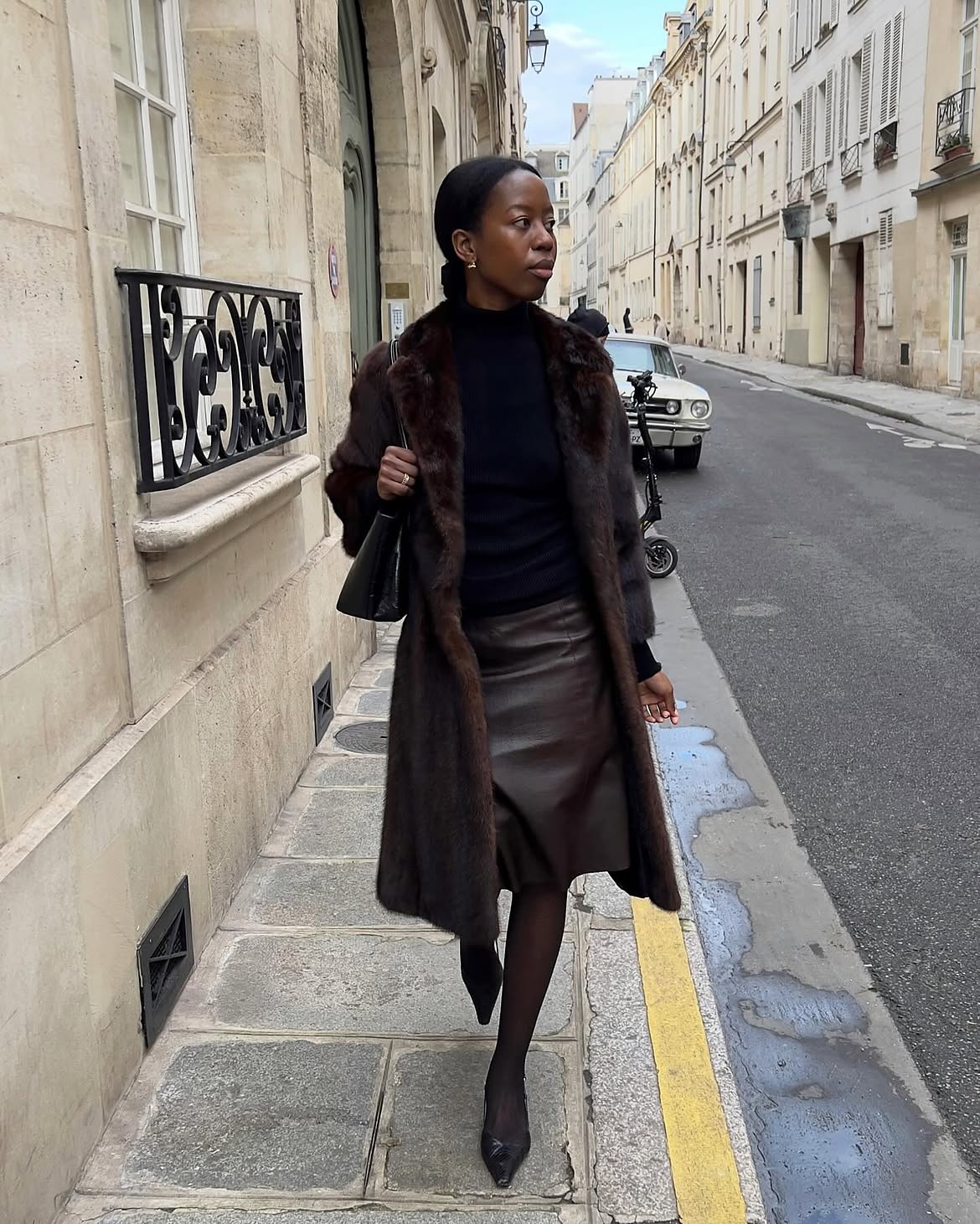 Woman wears a faux fur coat and a leather pencil skirt with a black jumper