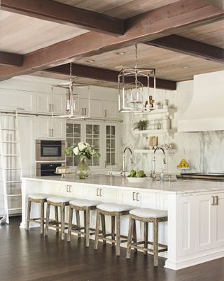 white traditional kitchen with central island with five bar stools and pendant lights on the ceilings are wooden beams and wooden ceiling