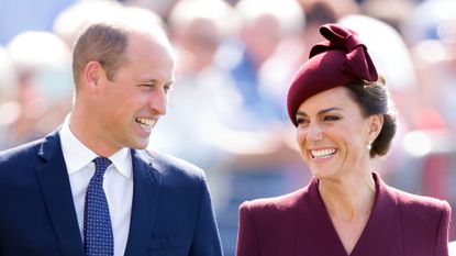 Kate Middleton wears a dark red coat and matching hat and Prince William wears a navy suit and matching blue tie