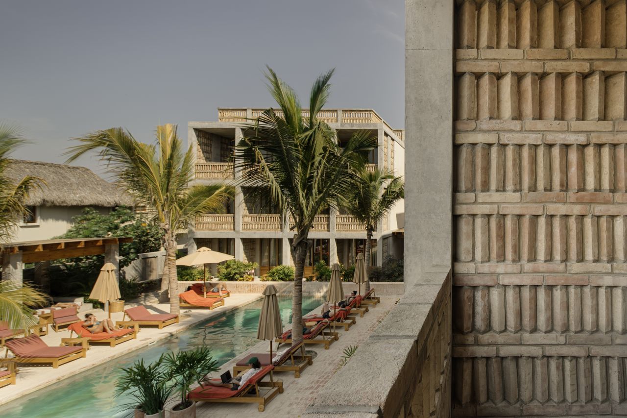 A Mexican brutalist hotel filled with palms, cement, terracotta tiles, and sun loungers.