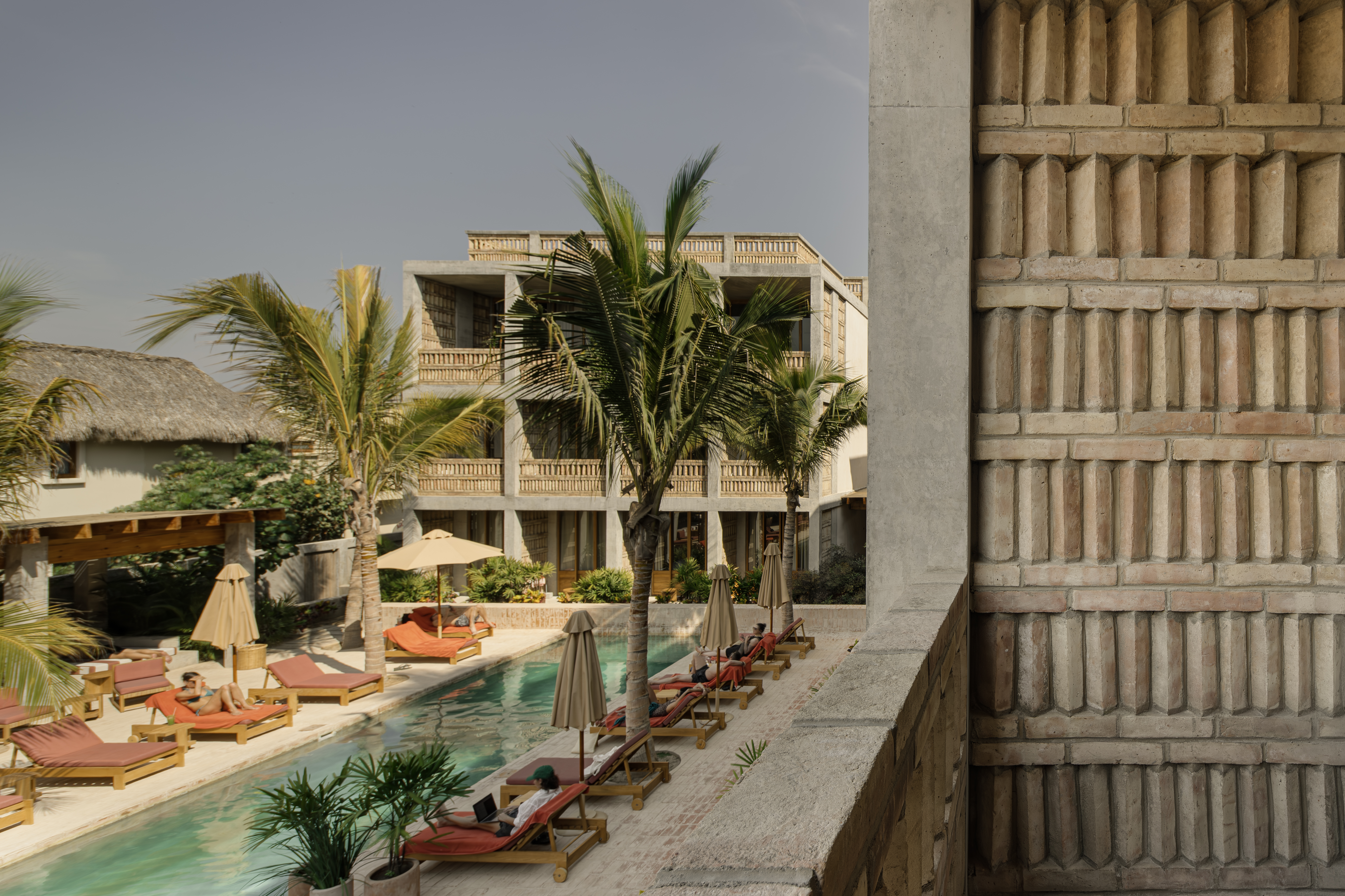 A Mexican brutalist hotel filled with palms, cement, terracotta tiles, and sun loungers.