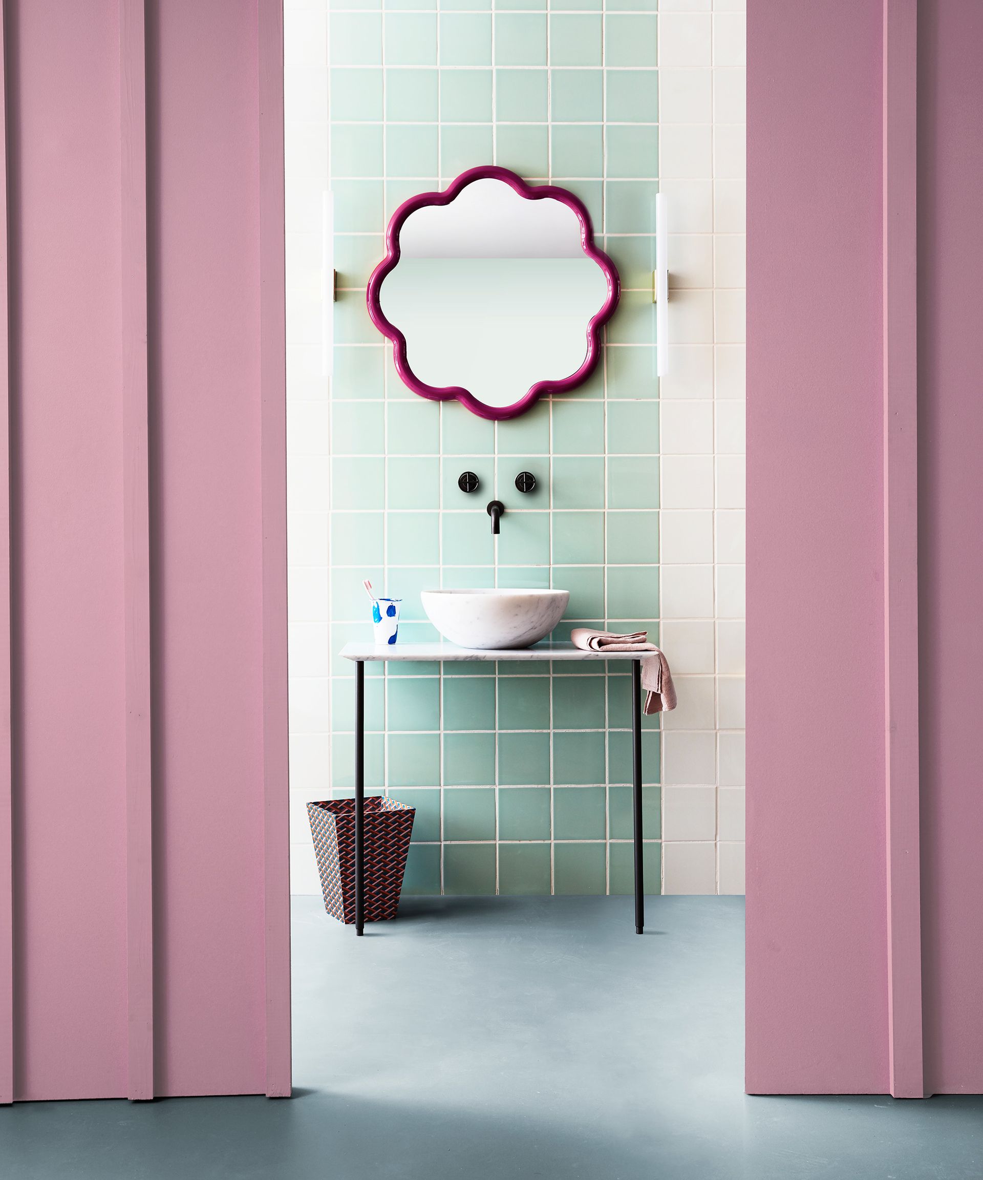 An example of bathroom color ideas showing a pink bathroom with green wall tiles and a flower shaped mirror
