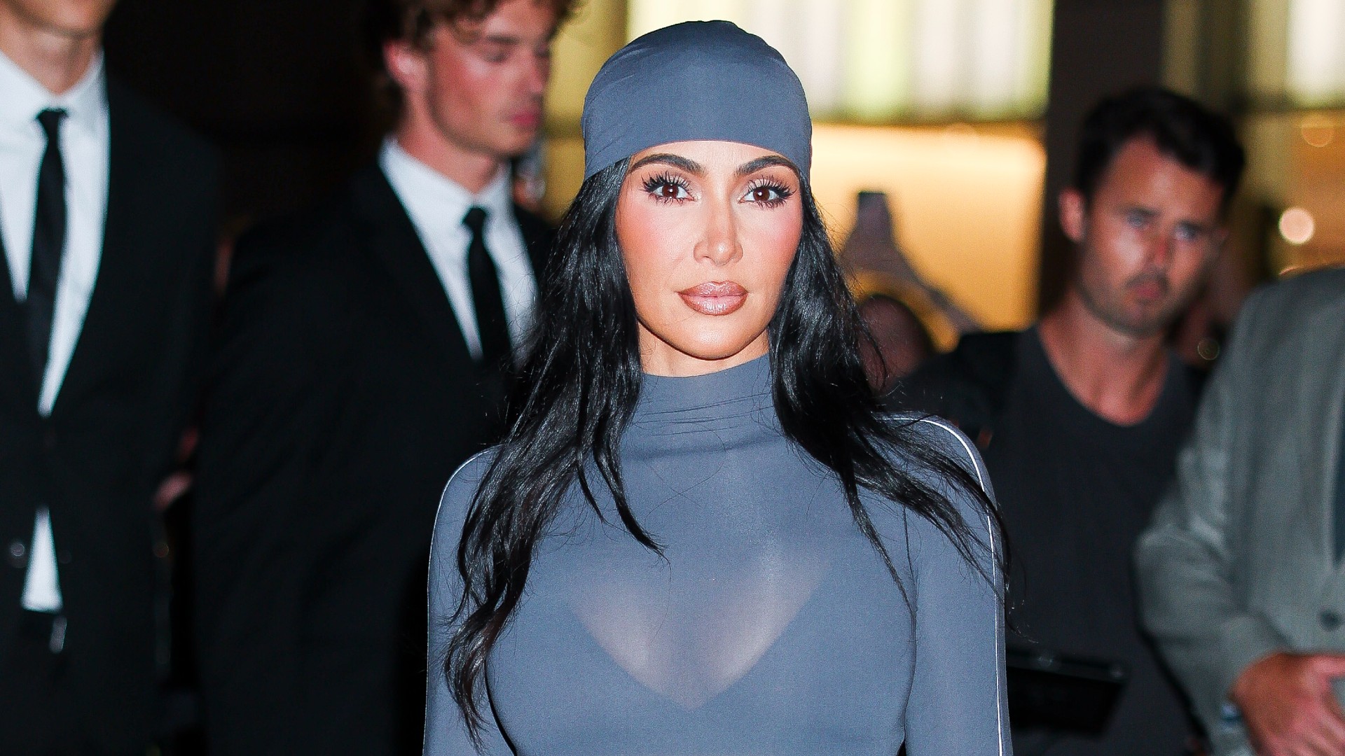 a paparazzi photo of a woman with long black hair wearing a gray scarf and a see through gray turtleneck top