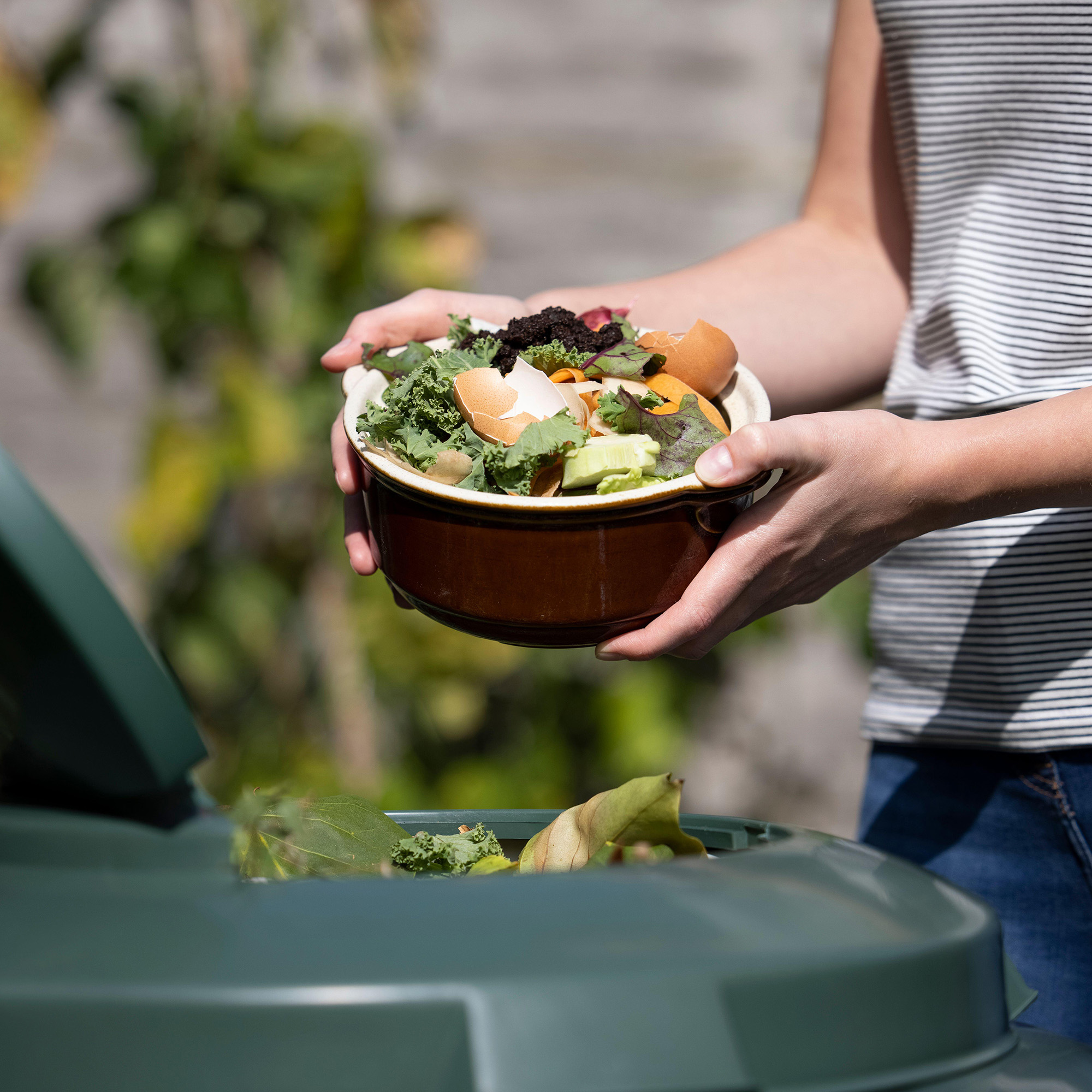 Close Up Of Woman Emptying Food Waste Into Garden Composter At Home