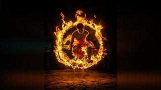 A performer leaps through a fiery ring, showcasing fire dancing skills against a dark background. Flames illuminate the scene dramatically