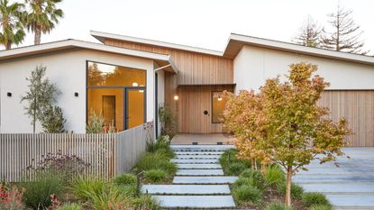 A front yard of a timber-clad house with irregular paving and grasses