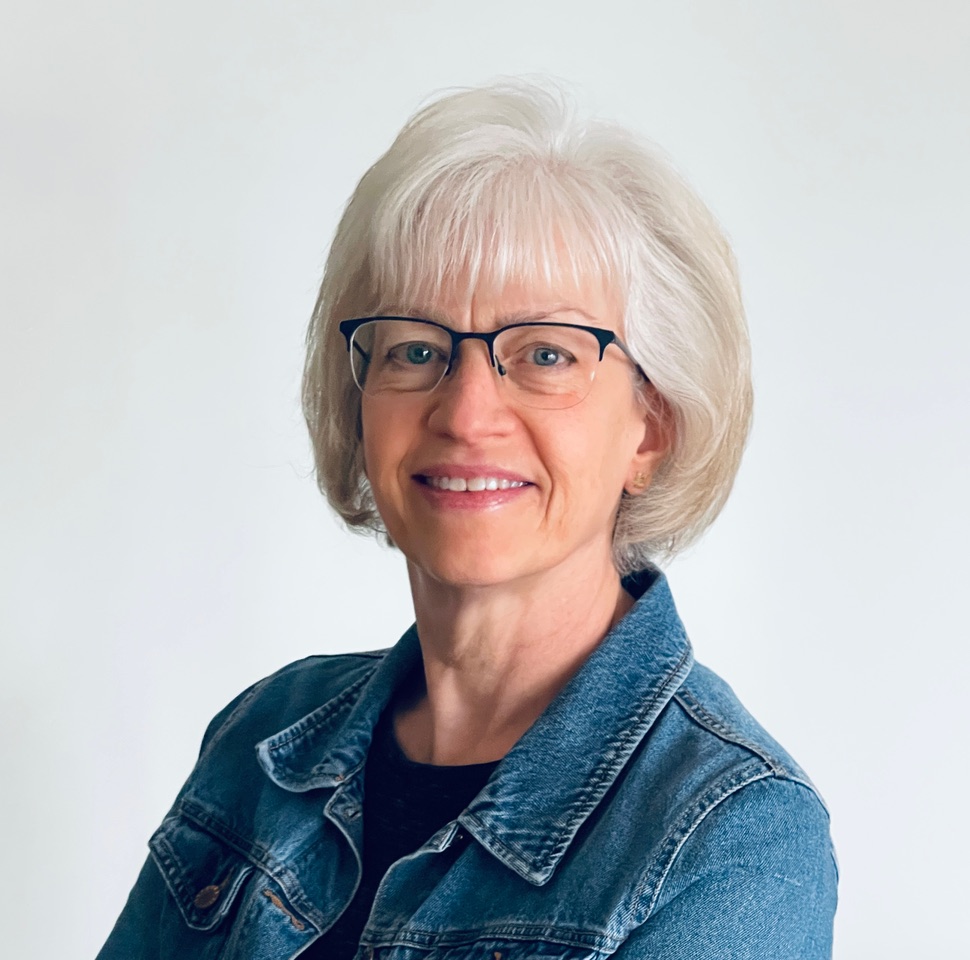Headshot of woman in blue denim jacket, with glasses and short white hair