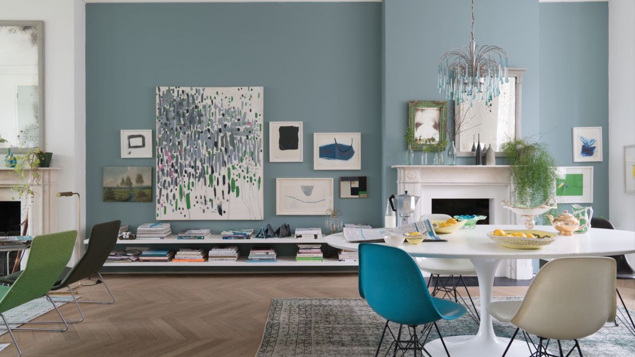 open plan dining room with mid-toned blue walls, parquet wood flooring, white round dining table with beige and bright blue chair