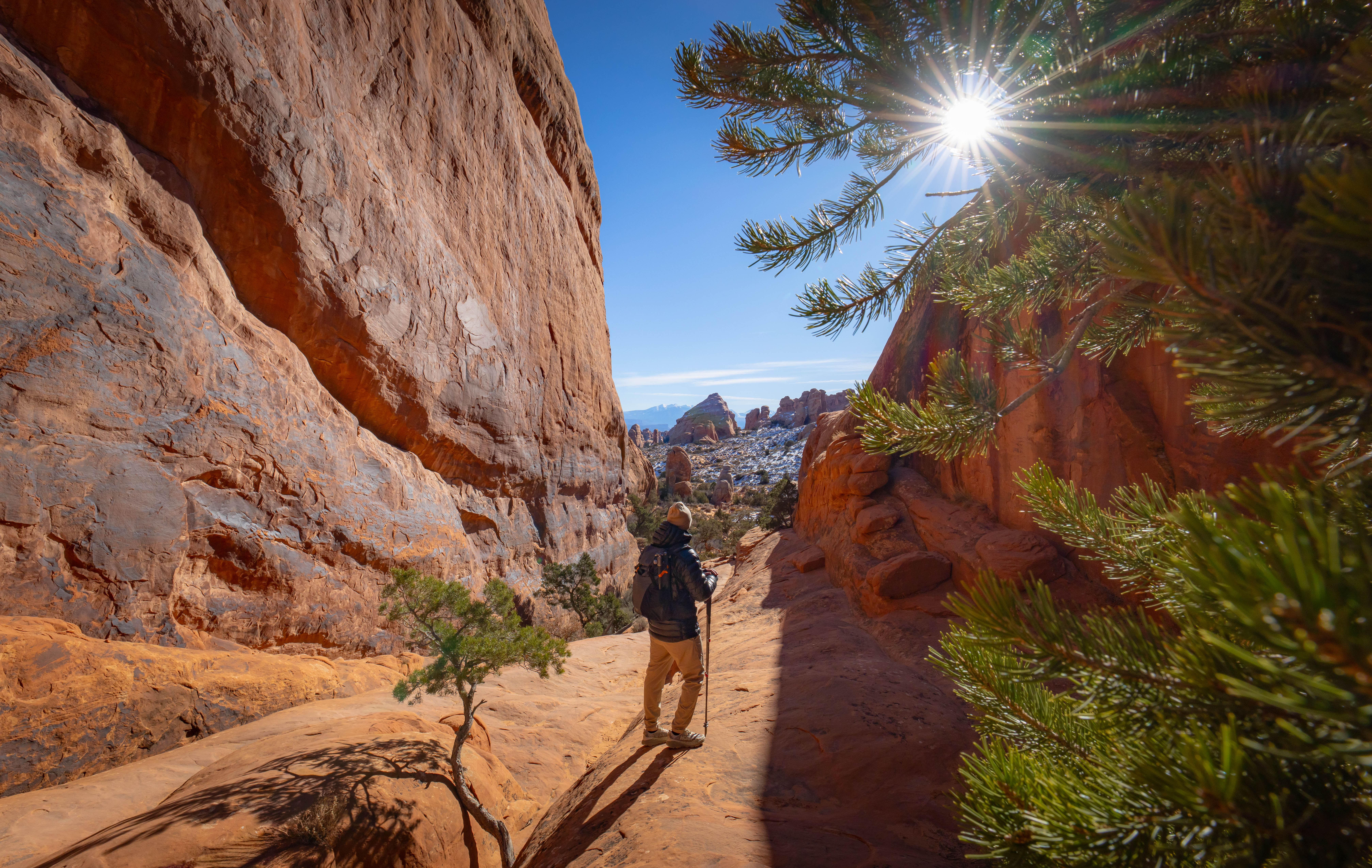 Sun shining through a stone archway in the desert with a hiker standing in the middle of the arch
