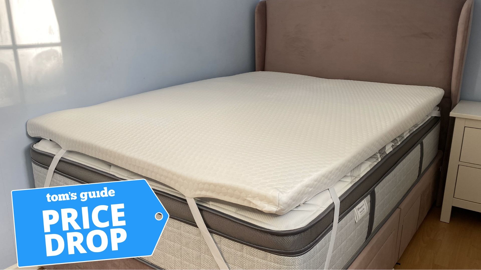 A &quot;Price drop&quot; deals badge sits in the corner of a picture of the Helix Premium Mattress Topper with GlacioTex strapped onto a bed. 
