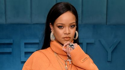 Rihanna wears a long-sleeved orange dress, large diamond hoop earrings, and has long straight black hair