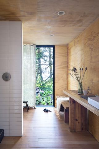 A bathroom with wooden panelling and a large window with a natural view