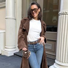 Influencer wearing white shirt, brown coat, sunglasses, and blue jeans standing on New York street.