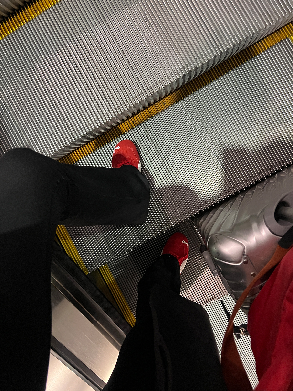Eliza Huber on an escalator at the airport with her Tumi suitcase and Longchamp tote bag wearing yoga pants and Puma Speedcat sneakers.