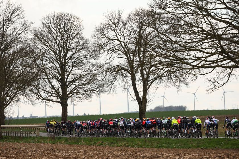 The pack of riders cycles with windmills in the background during the 2nd stage of the Paris-Nice cycling race, 183,9 km between Montesson and Bellegarde, on March 10, 2025. (Photo by Anne-Christine POUJOULAT / AFP)