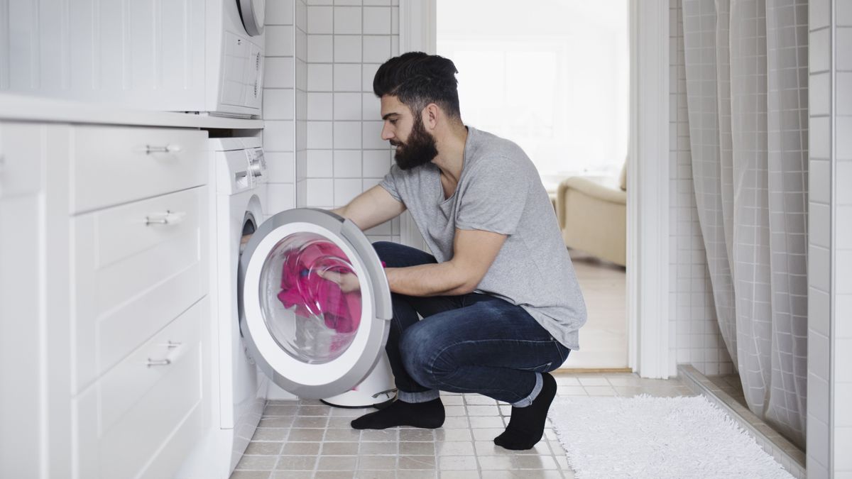 man with beard putting pink laundry in washer dryer -why is my washer-dryer not drying