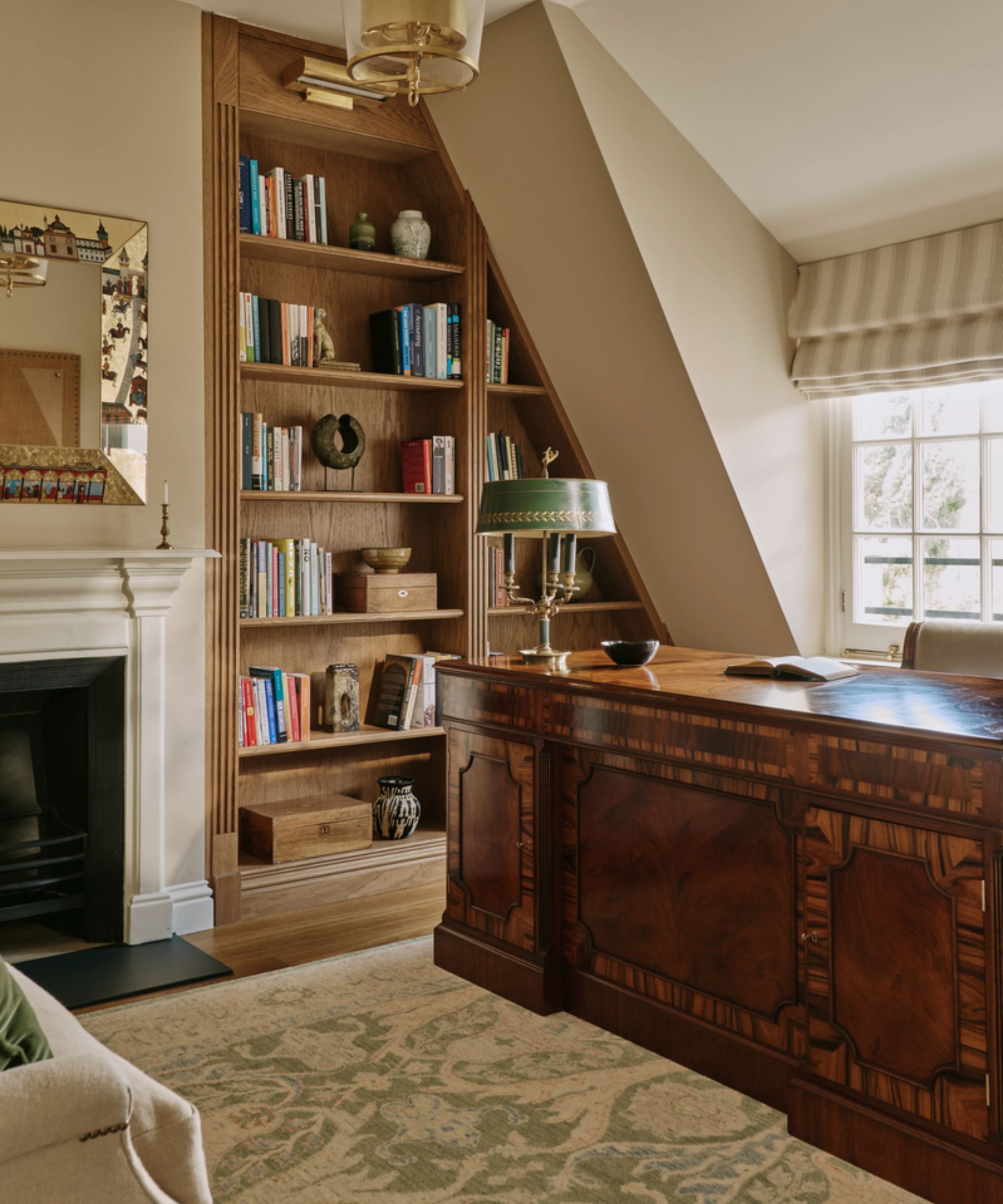 a cozy warm beige home office with a large antique wooden desk, original fireplace, vintage rug and built-in joinery