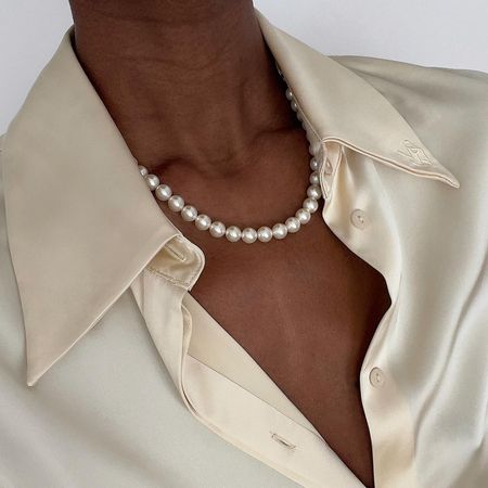 a woman wearing a cream satin top and a white pearl necklace