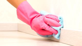 Pink rubber glove with blue cloth wiping down skirting board
